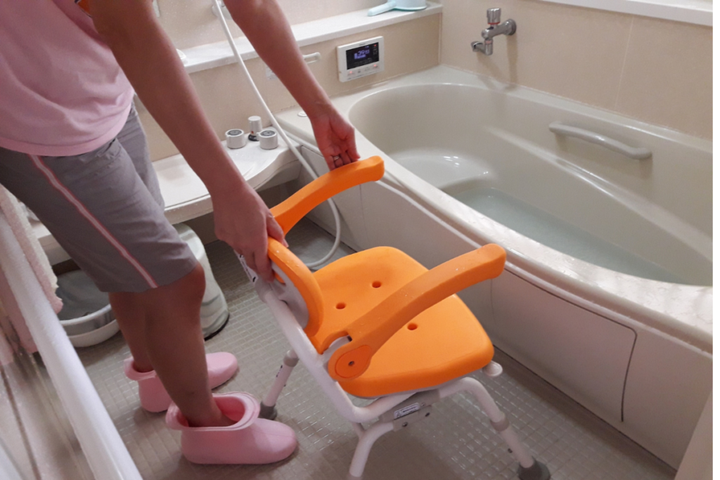 女性が浴室の洗い場にオレンジ色のシャワーチェアをセットしている写真